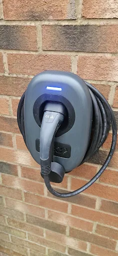 Dark home EV charger mounted on an exterior wall with the charging connector and cable attached, Leeds