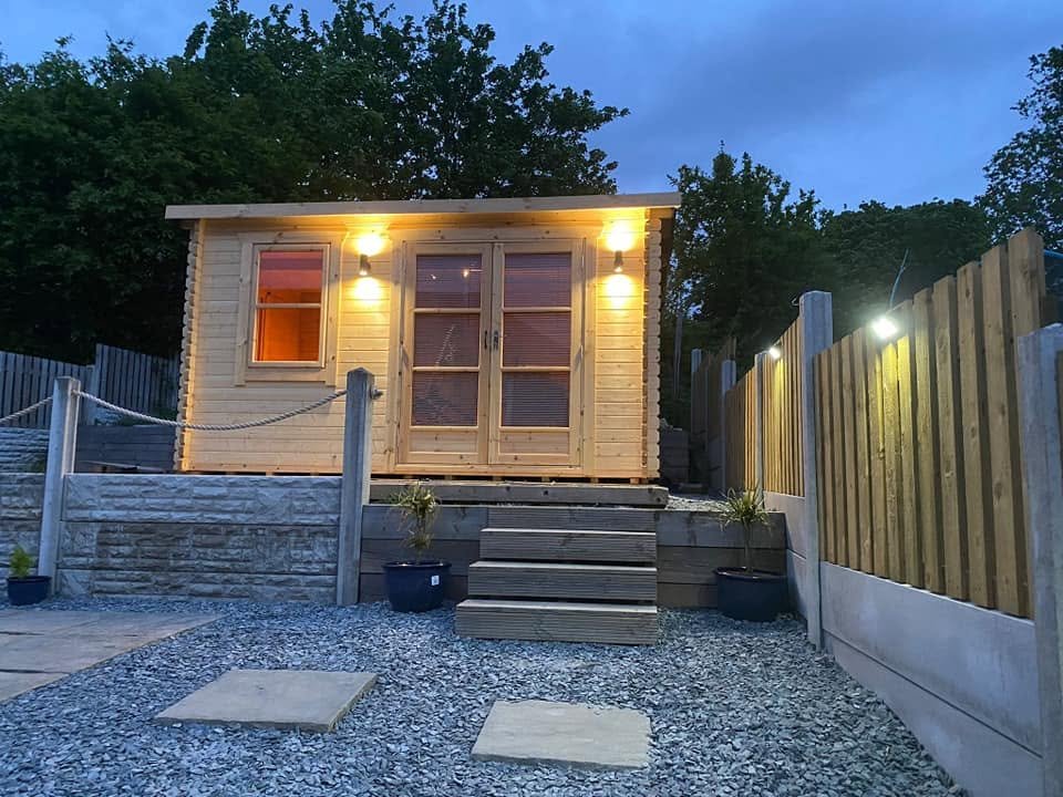 Timber summer house at dusk with exterior lights and garden fence lighting illuminated, Leeds