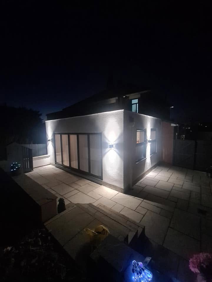 Modern house extension at night illuminated by architectural up/down exterior lighting either side of bifold doors, Leeds