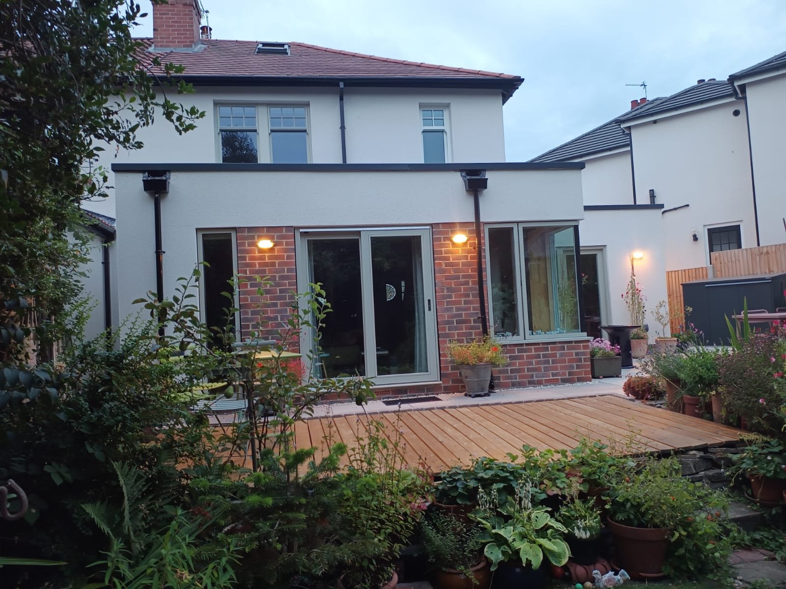 Rear single-storey extension at dusk with illuminated wall lights and timber decking, Leeds